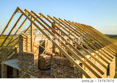 Unfinished brick house with wooden roof structure under construction. Unfinished brick house with wooden roof structure under construction. 74767679