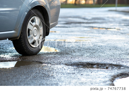 Close up of car wheel on a road in very bad condition with big potholes full of dirty rain water pools. Close up of car wheel on a road in very bad condition with big potholes full of dirty rain water pools. 74767738