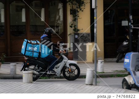 Thessaloniki, Greece Wolt food courier on motorbike speeding on city road. 74768822