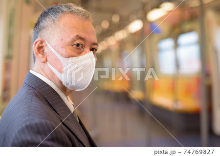 Mature Japanese businessman with mask thinking and sitting with distance inside the train 74769827