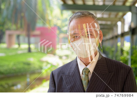 Mature Japanese businessman wearing mask and face shield at the park 74769984