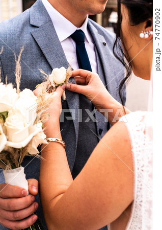 The bride puts a boutonniere on the groom's jacket on their wedding day. 74770902