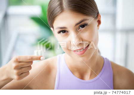 Beautiful young woman eating chewing gum, smiling 74774017