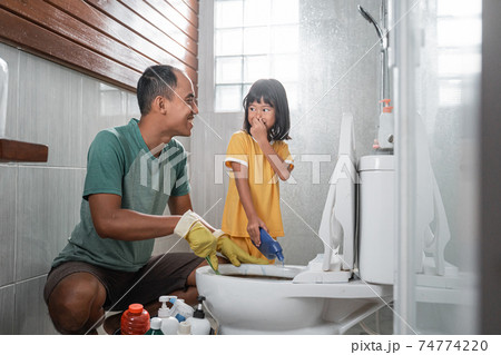 a father looks at each other with the little daughter who covers her nose while cleaning the toilet 74774220