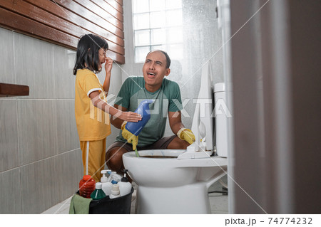 the little girl in a nasty pose holding a bottle of cleaning fluid chatting with her dad while brushing the dirty toilet the little girl in a nasty pose holding a bottle of cleaning fluid chatting with her dad while brushing the dirty toilet 74774232