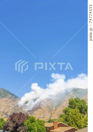 Clear blue sky over mountain slopes with puffs of smoke from a wild forest fire 74774333
