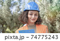 Portrait of a cheerful young woman engineer or worker in a uniform and protective blue hardhat, smiling and looking at camera at construction site 74775243