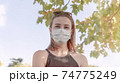 Portrait of young charming woman in medical mask looks at the camera, New normality after covid-19 pandemic. Outdoors shooting. Healthy lifestyles 74775249