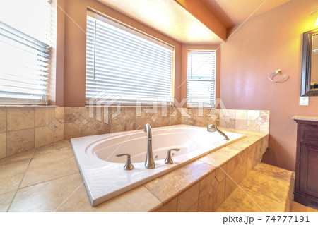 Elevated built in bathtub against the bay windows with blinds of a bathroom 74777191