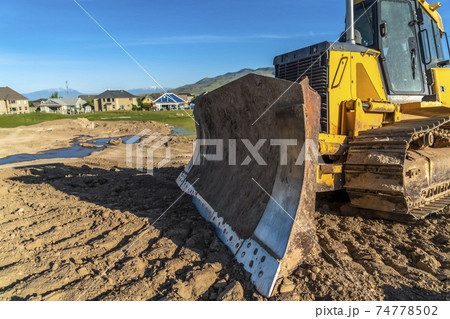 Close up of a bulldozer with metal blade yellow paint and tracks with dried mud 74778502