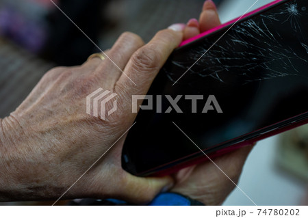 ひび割れたスマホを持つシニアの手 74780202