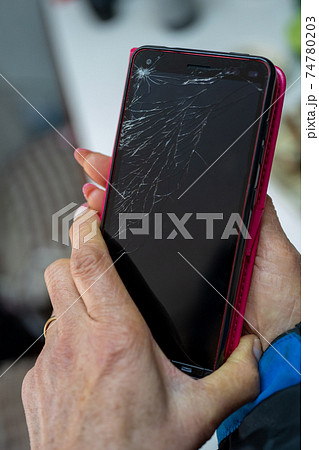 ひび割れたスマホを持つシニアの手 74780203