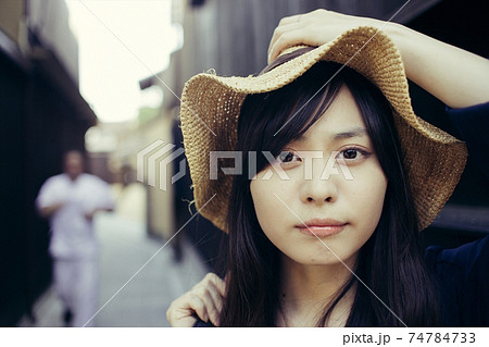 麦わら帽子を押さえるロングヘアの女性 カメラ目線の写真素材