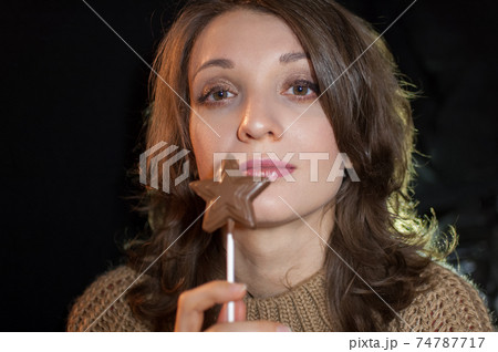 Female portrait of a girl holding chocolate star on stick and looking at the camera on black background in studio. Diet and food concept 74787717