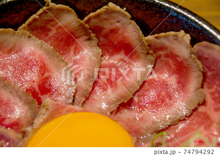 霜降り牛肉のスライスで埋め尽くされたローストビーフ丼、卵黄トッピング。薬味刻みネギ、大根おろし。 霜降り牛肉のスライスで埋め尽くされたローストビーフ丼、卵黄トッピング。薬味刻みネギ、大根おろし。 74794292