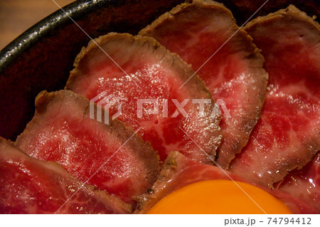 霜降り牛肉のスライスで埋め尽くされたローストビーフ丼、卵黄トッピング。薬味刻みネギ、大根おろし。 霜降り牛肉のスライスで埋め尽くされたローストビーフ丼、卵黄トッピング。薬味刻みネギ、大根おろし。 74794412