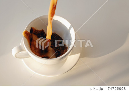 Pouring of coffee in a cup creating splash Pouring of coffee in a cup creating splash 74796098