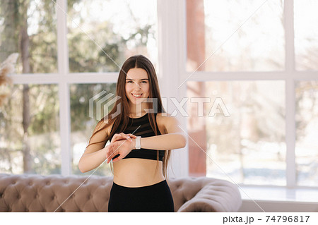 Attractive young woman training at home. Girl have a break and look at watch. Happy female use dumbbells for training 74796817