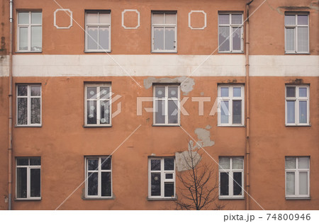 A part of yellow brown building facade with windows and a tree in front of it. Street view cityscape of Klaipeda city in Litrhuania. Retro hipster faded style of processing. Grey and gloomy mood. A part of yellow brown building facade with windows and a tree in front of it. Street view cityscape of Klaipeda city in Litrhuania. Retro hipster faded style of processing. Grey and gloomy mood. 74800946