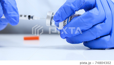Female doctor hands in blue medical gloves with transparent liquid coronavirus vaccine bottle and syringe for injection in the laboratory. Research and development of new cure for diseases 74804302