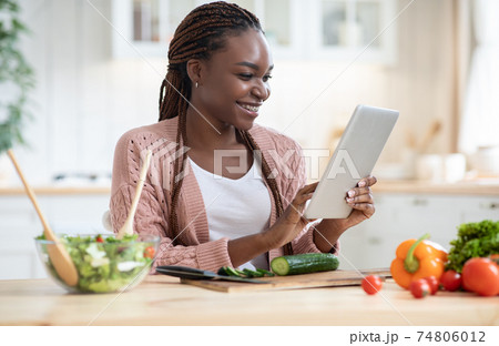 Online Recipe. Cheerful african woman using digital tablet in kitchen while cooking 74806012