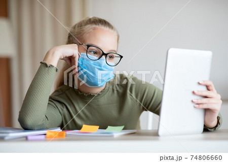 Bored teen girl in face mask using digital tablet 74806660