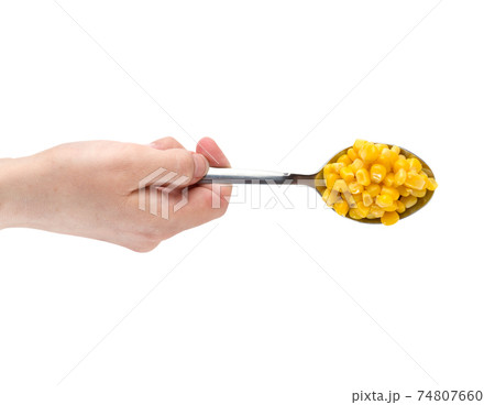 Canned corn on a white background. A hand holds an iron spoon of canned corn close up. 74807660