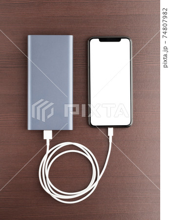 Power bank and smartphone on wooden table. The smartphone is charging from the power bank. 74807982
