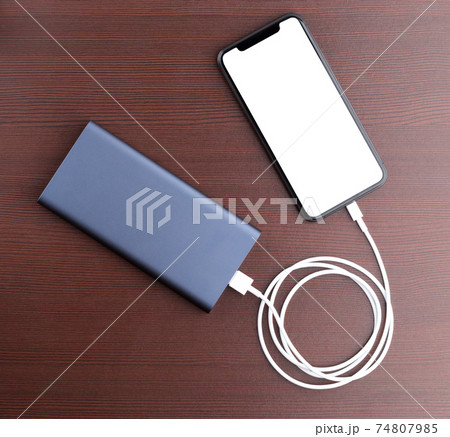 Power bank and smartphone on wooden table. The smartphone is charging from the power bank. 74807985