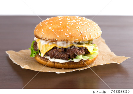 Burger on parchment paper. Beef patty burger, cheddar cheese, lettuce, bacon, tomato and balsamic sauce. 74808339