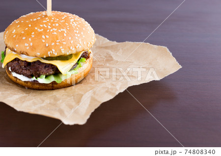 Burger on parchment paper. Beef patty burger, cheddar cheese, lettuce, bacon, tomato and balsamic sauce. Burger on parchment paper. Beef patty burger, cheddar cheese, lettuce, bacon, tomato and balsamic sauce. 74808340