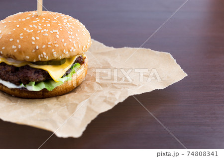 Burger on parchment paper. Beef patty burger, cheddar cheese, lettuce, bacon, tomato and balsamic sauce. 74808341