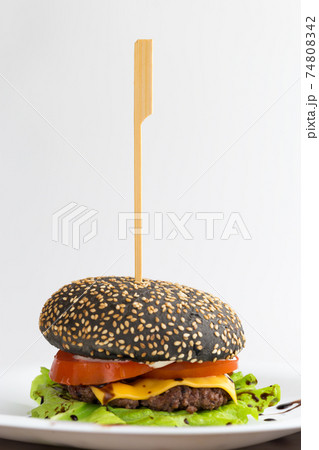 Black burger on a white plate. Beef patty burger, cheddar cheese, lettuce, bacon, tomato and balsamic sauce. The bun is made with the addition of ink cuttlefish. 74808342