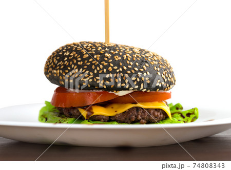 Black burger on a white plate. Beef patty burger, cheddar cheese, lettuce, bacon, tomato and balsamic sauce. The bun is made with the addition of ink cuttlefish. 74808343