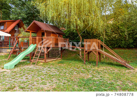 Empty modern wooden children playground set on green yard in public park in summer day. Funny toy land for kids. Urban exercise activities for child outdoors. Neighborhood childhood concept. Empty modern wooden children playground set on green yard in public park in summer day. Funny toy land for kids. Urban exercise activities for child outdoors. Neighborhood childhood concept. 74808778