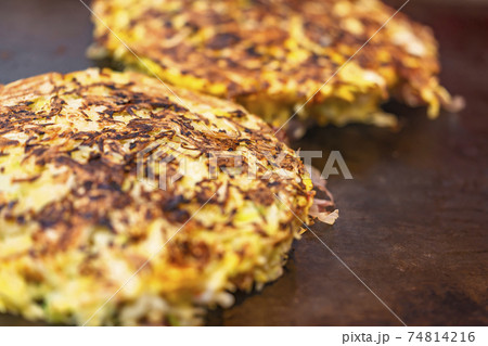 [国内] 鉄板で焼いてる調理中のひっくり返されたお好み焼きのクローズアップ 74814216