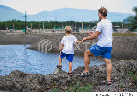 Father and son walk along man made breeding fish lake mountain background. Happy childhood. Home natural child education, fathers day, dad responsibilities, influence on son worldview formation 74817466