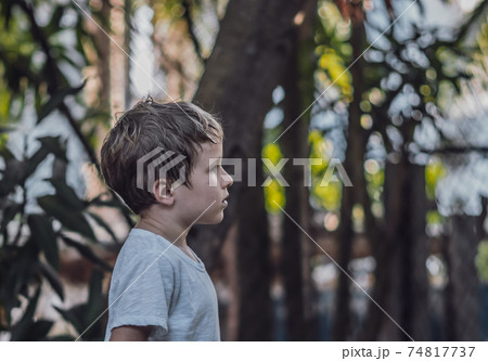 Side view kid child six year boy looking straight serious sad in white t-shirt outside nature background. Dark mood, childhood parenthood psychology education problems crisis due COVID concept Side view kid child six year boy looking straight serious sad in white t-shirt outside nature background. Dark mood, childhood parenthood psychology education problems crisis due COVID concept 74817737
