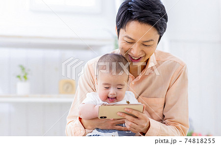 スマホを赤ちゃんに見せてあやすパパ スマホを赤ちゃんに見せてあやすパパ 74818255