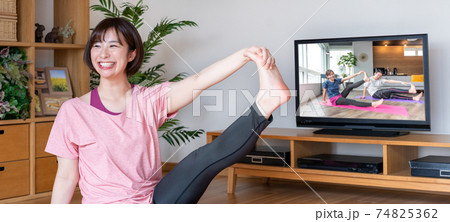 オンラインヨガ　リビングでストレッチをする若い女性　バナーサイズ 74825362