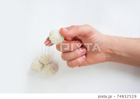 Male hand holds white chocolate candy on white background. Handmade candies, Sweet balls. Isolated background. Selective focus. 74832529