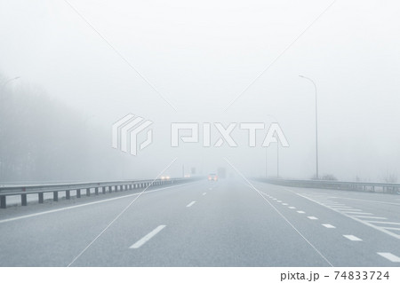 Driver POV of almost empty grey foggy misty rainy highway intercity road with low poor visibility on cold spring autumn morning. Seasonal bad rainy weather accident danger warning. car fog light Driver POV of almost empty grey foggy misty rainy highway intercity road with low poor visibility on cold spring autumn morning. Seasonal bad rainy weather accident danger warning. car fog light 74833724