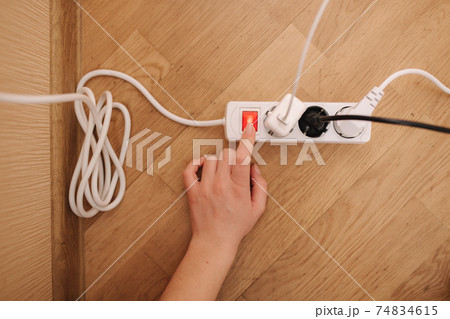 Top view of female hand turn on the extension cord at home. White cable connector Top view of female hand turn on the extension cord at home. White cable connector 74834615