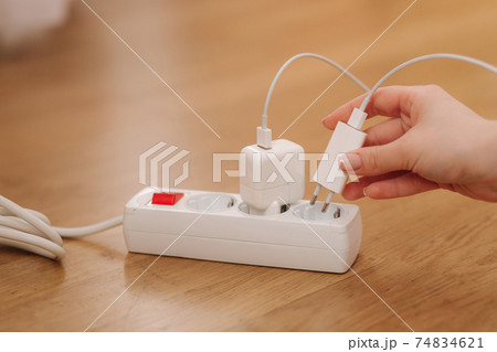 Woman pluging the wire into white extension cord. Close up of female hand put cabel 74834621