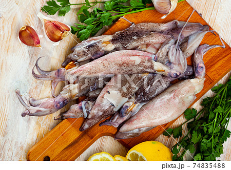 Uncooked squid with lemon and parsley on a wooden cutting board 74835488