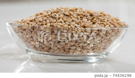 Barley groats in glass bowl on white surface , nobody Barley groats in glass bowl on white surface , nobody 74836296