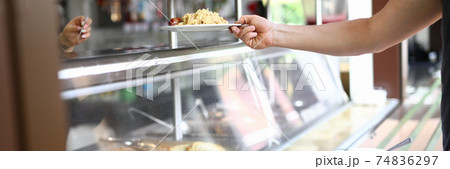 Man stand behind counter of ready-made food in dining room and hold plate with lunch in his hand. Man stand behind counter of ready-made food in dining room and hold plate with lunch in his hand. 74836297