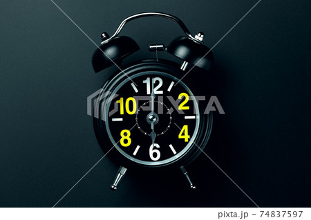 A stylish black alarm clock with yellow and white numbers stands on a dark background. Blank for the A stylish black alarm clock with yellow and white numbers stands on a dark background. Blank for the 74837597