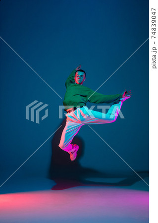 Stylish sportive boy dancing hip-hop in stylish clothes on colorful background at dance hall in neon light. Youth culture, movement, style and fashion, action. 74839047