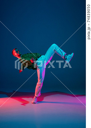 Stylish sportive boy dancing hip-hop in stylish clothes on colorful background at dance hall in neon light. Youth culture, movement, style and fashion, action. 74839050